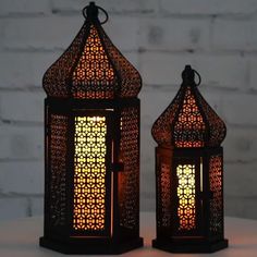 two decorative lanterns sitting next to each other on top of a white table with a brick wall in the background