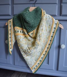 a green and yellow shawl hanging from a hook on a blue cabinet with wooden handles