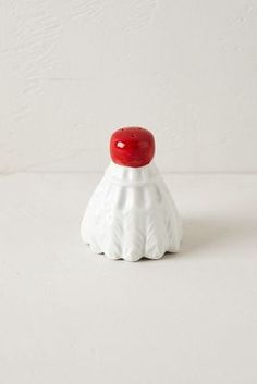 a small white vase with a red lid on it's side sitting on a table