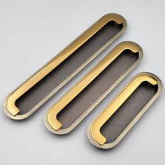 three metal handles on a gray surface with gold trimmings and black felt backing