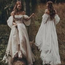 two women in white dresses standing next to each other on the grass with trees in the background