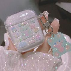 a person holding an airpods case with glitters on it and a keychain attached