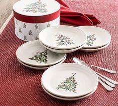 four white plates with christmas trees on them next to a red and white gift box