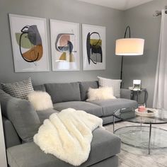 a living room with gray couches and pictures on the wall above them, along with a round glass coffee table