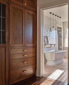 a bathroom with wooden cabinets and white bathtub next to an open door that leads to another room