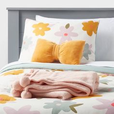 a bed with pink and yellow flowers on the comforter, two throw pillows and one blanket