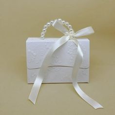 a small white box with a ribbon tied around it and some pearls on the side