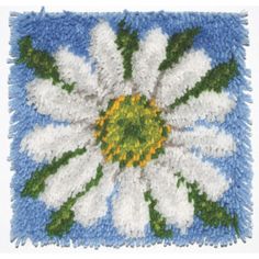 a white and green flower is on a blue square with grass in the center that looks like it's made out of yarn