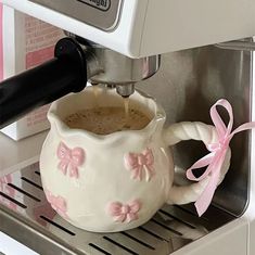 a white coffee pot with pink bows on it next to an espresso machine