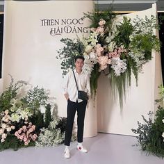 a man standing in front of a floral display at a fashion show with flowers and greenery