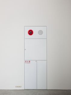 a white door with a red button on the side in an empty room next to a wall