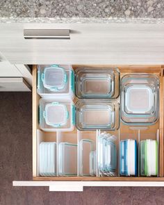 an open drawer filled with glass containers and dishes on top of a counter next to a stove