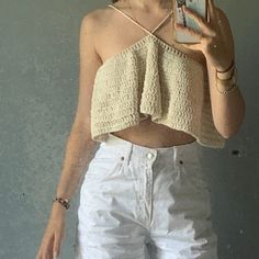 a woman taking a selfie in front of a mirror wearing white shorts and a crocheted crop top