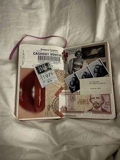 an open book with pictures and stamps on it sitting on a bed covered in white sheets