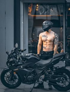 a shirtless man standing next to a motorcycle in front of a storefront window