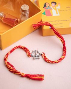 an orange and yellow bracelet with two silver anchor charms on it next to a box