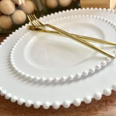 two white plates with gold forks on them sitting on a wooden table next to some balls