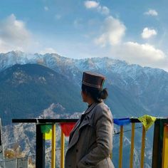 a woman standing on top of a mountain next to a rainbow colored railing with mountains in the background