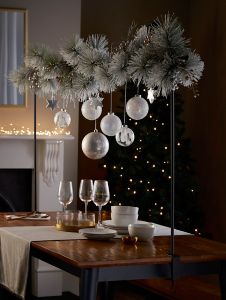 a dining room table set for christmas with ornaments hanging from the ceiling and candles in front of it