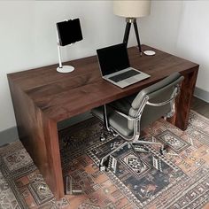 a laptop computer sitting on top of a wooden desk next to a lamp and chair