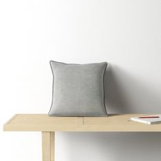 a gray pillow sitting on top of a wooden table next to a book and pen