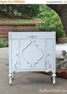 a white cabinet sitting on top of a sidewalk next to a brick planter and tree