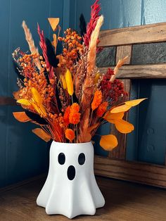 a white vase filled with lots of different colored flowers and plants next to a wooden bench