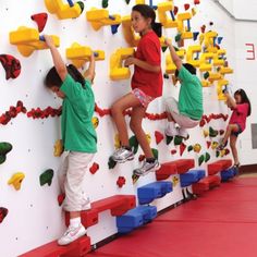 three children climbing up and down a rock wall with colorful blocks on the walls behind them