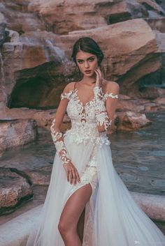 a woman in a white dress standing next to a waterfall wearing high heels and holding her hand up to her face