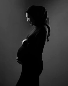 a pregnant woman wearing a hijab and holding her belly in black and white