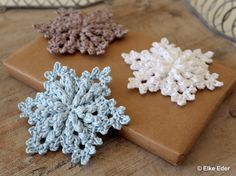 three crocheted snowflakes sitting on top of a cutting board next to each other