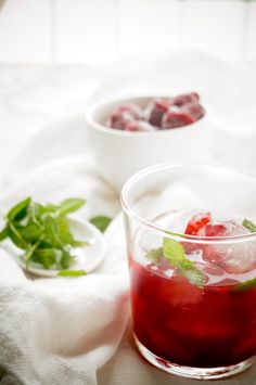 two glasses filled with red liquid and garnished with mint on a white cloth