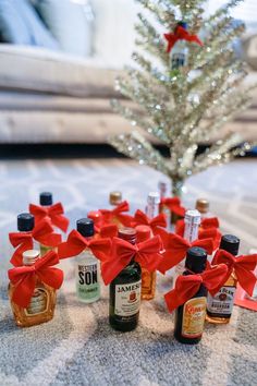 bottles of liquor tied with red ribbon on the floor next to a small christmas tree