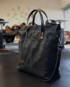 Tote bag with luggage handle attachment in American heavy weight waxed canvas. The color is black for the body and black leather bottom. I made it into an everyday bag perfect for the office, with leather handles, shoulder strap, and 3 outside pockets Closing with a zipper on top. And on the backside a luggage handle attachment Including a leather shoulder strap, adjustable and detachable. Fully lined with a cotton canvas and double inside pockets. All the bags are made and designed by myself an Luxury Coated Canvas Bag With Gunmetal Hardware, Black Shoulder Bag With Leather Handles For Commuting, Black Canvas Weekender Bag With Leather Handles, Black Weekender Bag With Canvas Lining For Daily Use, Black Waxed Canvas Tote Shoulder Bag, Black Waxed Canvas Shoulder Bag With Leather Trim, Black Waxed Canvas Satchel With Leather Handles, Black Waxed Satchel For Daily Use, Black Travel Briefcase With Waxed Finish