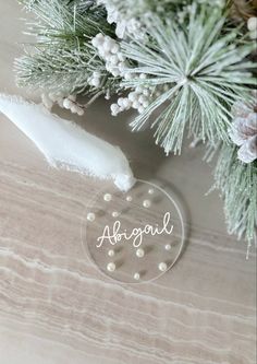 a glass ornament with the word abogal on it next to some pine branches