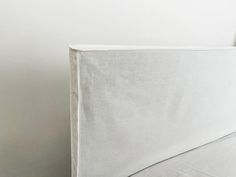 an unmade bed with white sheets and pillows on it's headboard, against a plain white wall