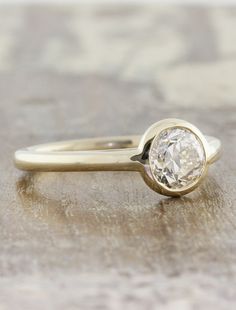 a yellow gold engagement ring with a round diamond in the center on a wooden surface