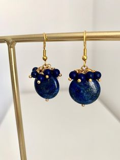 These gorgeous earrings feature a fabulous combo of gold and navy blue cluster beads, creating a captivating and eye-catching design. With their elegant round teardrop Lapis lazuli gemstone measuring 2cm and dainty 4mm round beads, these earrings are the perfect accessory to update any look effortlessly. The deep navy blue color of the Lapis Lazuli gemstone, known for its association with strength and courage, adds a touch of royalty and wisdom to this piece. The total height of the earrings, including the earwires, is 4.00cm (1.57 inches). Crafted with high-quality stainless steel gold pins and wire, these earrings are not only stylish but durable too. Each pair is thoughtfully presented in a charming gift box, making it an ideal choice for a special someone or a well-deserved treat for y Blue Gemstone Bead Drop Earrings, Blue Gemstone Beads Drop Earrings, Blue Round Earrings With Gemstone Beads, Gold Earrings With Gemstone Beads, Gold Earrings With Natural Lapis Lazuli Stones, Lapis Lazuli Dangle Earrings With Natural Stones, Lapis Lazuli Natural Stones Drop Earrings, Blue Gold Earrings, Royal Blue Earrings