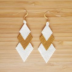 the beaded earrings are made with white and gold beads, on a wooden surface