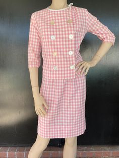 1960s two piece suit. Pink and white gingham cotton. Eight button front top; four functional. White trim at neck has decorative white bow. Snap fastener at neck. Skirt has elastic waist. Measurements  Top 38" bust 36" hem 21" length 15" sleeves 14" shoulders Skirt 20"-32" elastic waist 38" hips 21" length Cute suit shows well exhibiting very minimal to no wear. Pastel Office, Retro Pink Button-up Blouse, Vintage Pink Collared Dress, Vintage Pink Button-up Blouse, Suits Show, Vintage Pink Dress With Button Closure, Pink Outerwear With Lapel Collar And Double-breasted Fastening, Rock Hat, White Two Piece