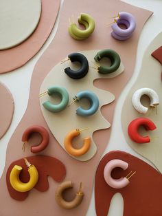 several pairs of colorful earrings on top of a white surface with pink, blue, yellow and green shapes