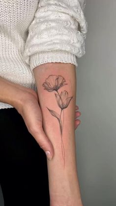 a woman's arm with a small flower tattoo on the left side of her forearm