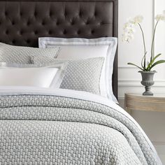 a bed with white and gray comforters in a bedroom next to a vase filled with flowers