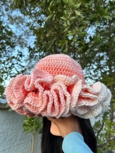 a woman wearing a pink crocheted hat with large ruffles on it