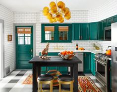 a kitchen with green cabinets and black countertops, gold stools and an area rug