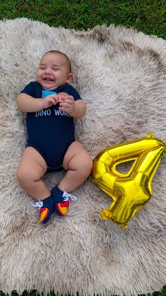 a baby laying on top of a white rug next to a yellow letter shaped balloon