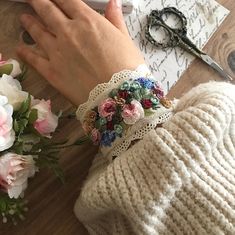 a woman's hands with flowers and scissors on a table next to some paper