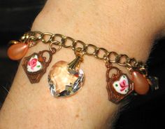 "Antique Vintage Crystal Heart & Guilloche Red Enamel Charm Bracelet 7 3/8\" Dainty gold finish link bracelet features 1920's - 1950's charms, which include: a large faceted crystal heart, 2 embossed copper purse / handbag shape charms with hand painted rose enamel hearts, 4 peach color faux pearl drops, 2 red guilloche enamel hearts, and 4 dangling Aurora Borealis crystal beads. Sweet and feminine! Don't miss this chance at a one-of-a-kind piece! Unmarked Measures approximately 7 3/8\" long Vintage Adjustable Heart Bracelet As Gift, Vintage Adjustable Heart Bracelet For Gift, Adjustable Vintage Heart Bracelet For Gift, Vintage Heart Charm Bracelet As A Gift, Vintage Heart Charm Bracelet For Anniversary, Vintage Bracelets With Heart Beads For Gift, Vintage Heart Charm Bracelet For Gift, Vintage Red Jewelry With Heart Charm, Vintage Heart-shaped Bracelets For Gifts