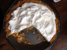 a pie with white frosting on top is sitting on a table next to a cup