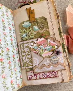 an open book with papers and flowers on the pages next to some scissors, tape and other crafting supplies